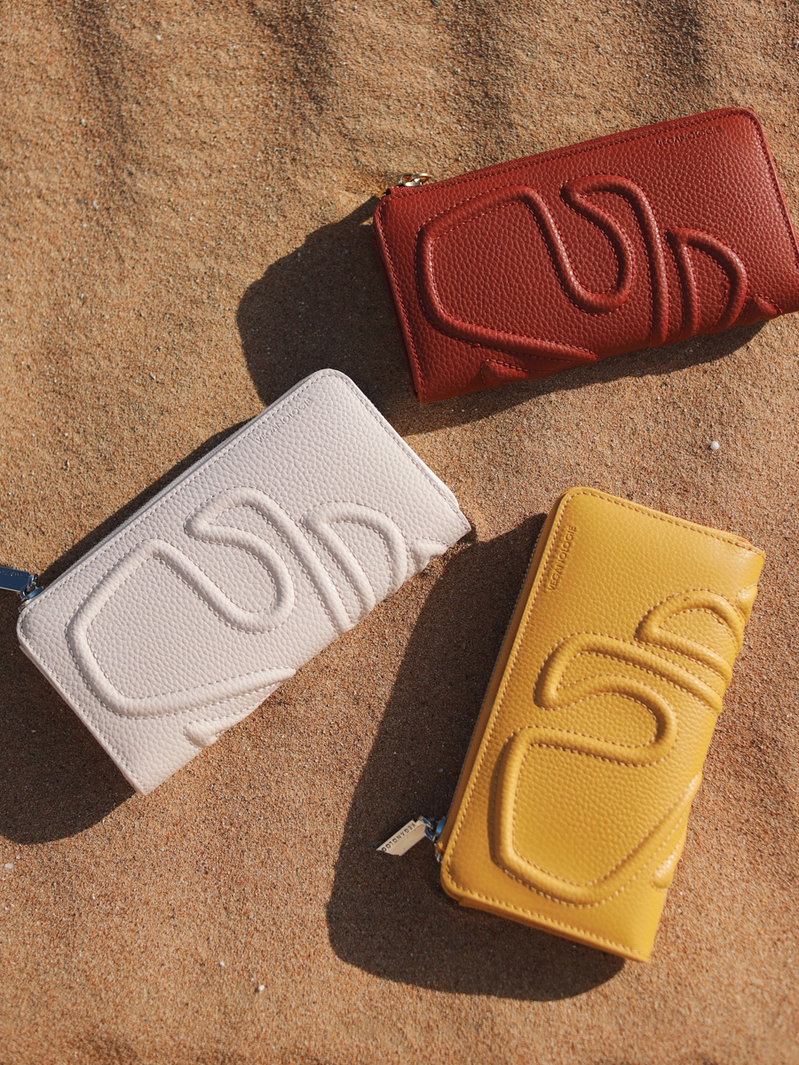 Close-up of three Veganologie purses displayed on sand